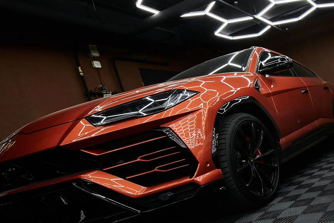 Передняя часть и колесо оранжевого Lamborghini Urus на чёрном модульном полу