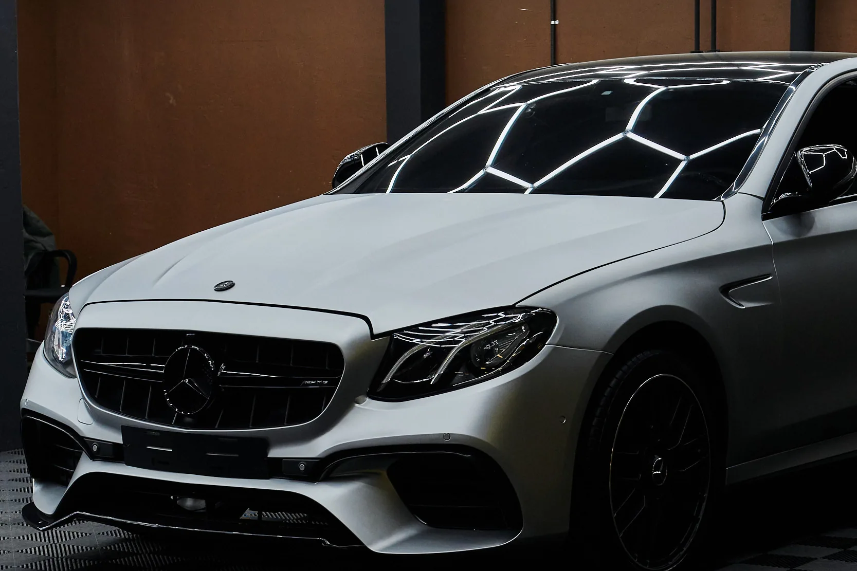 Седан Mercedes-AMG в сатиновой плёнке у терракотовой стены, световые соты отражаются в крыше