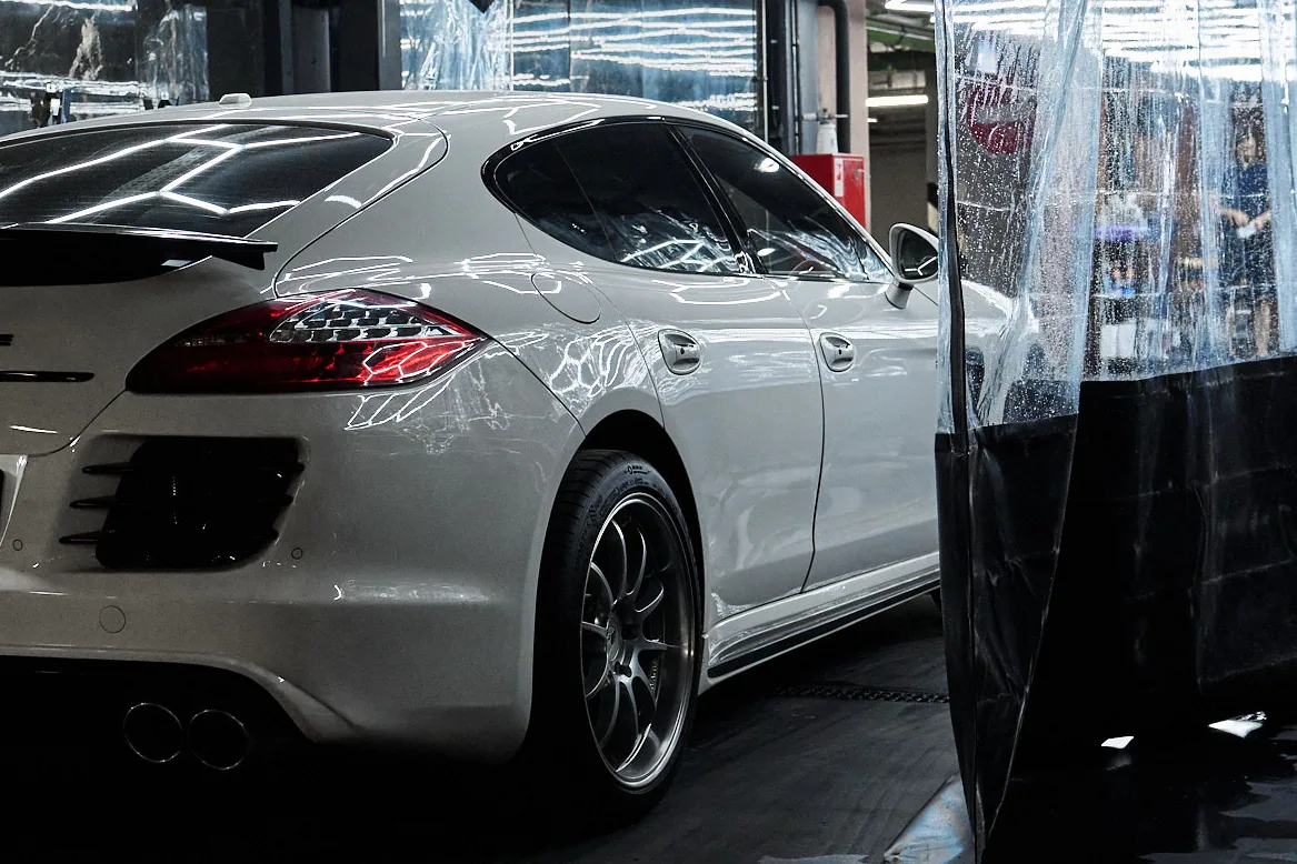 Корма белого Porsche Panamera у прозрачной ПВХ-шторы, световые соты отражаются в крыле
