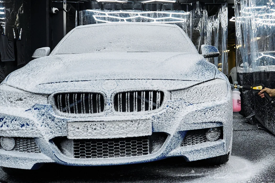 Седан BMW целиком под слоем снежной пены, над ним светится сотовый потолок