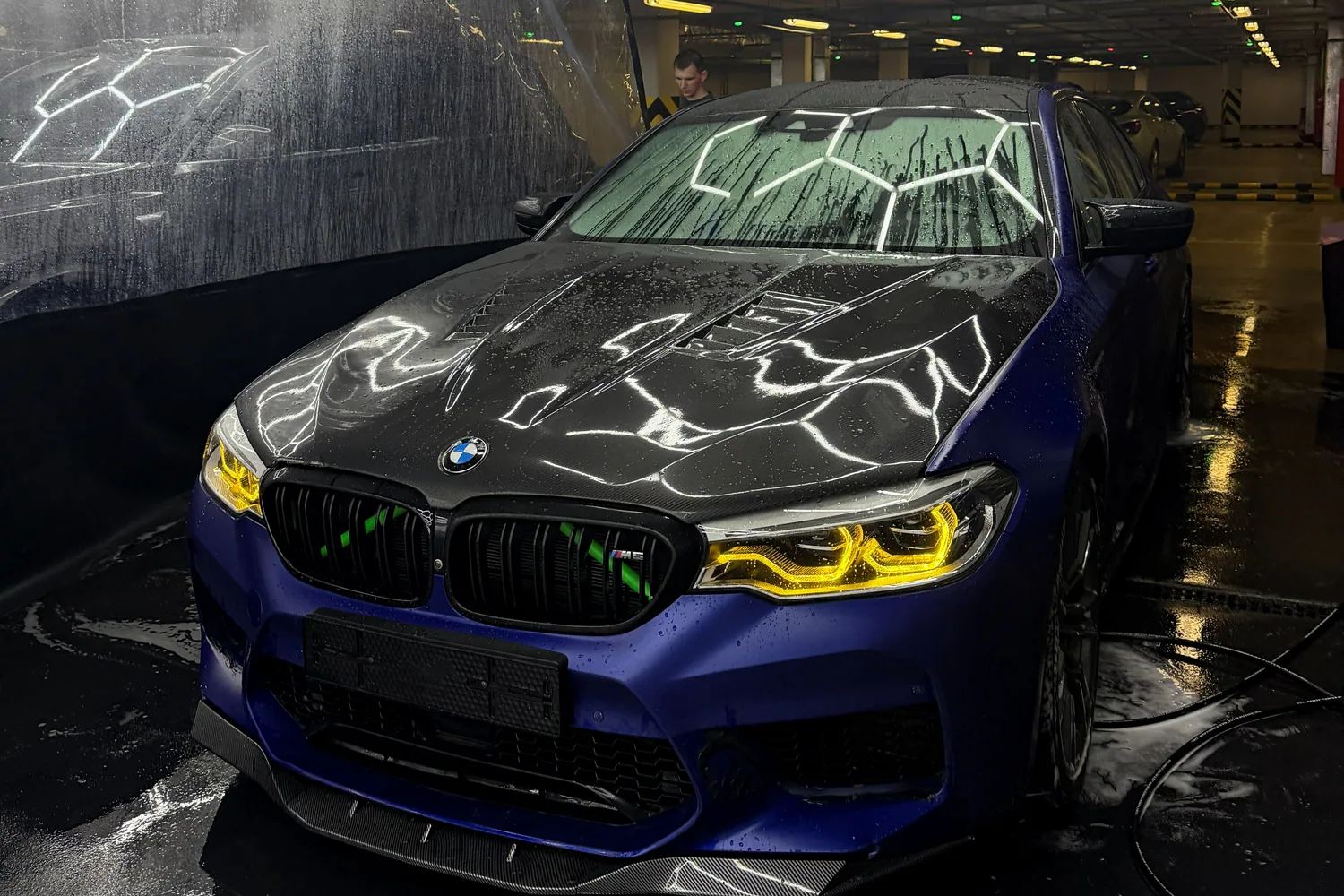 Синий BMW с карбоновым капотом под светом моечного бокса